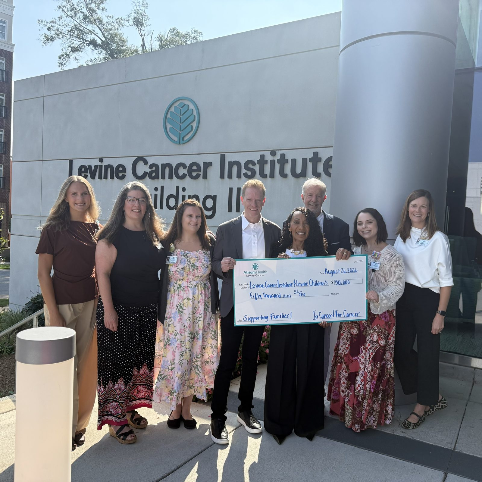 A group from In Concert for Cancer and Atrium Health holding a ceremonial $50,000 check made out to Levine Cancer Institute and Levine Children’s, outside the Levine Cancer Institute Building III entrance.